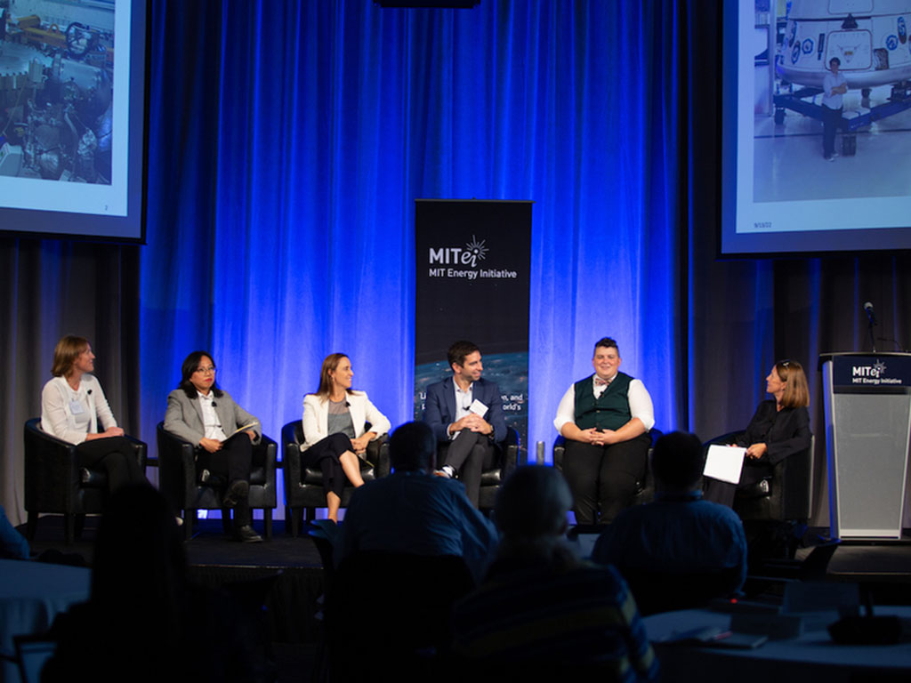 Five panelists sit in a row on stage with a moderator.