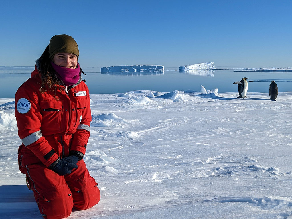 MIT Student Lock Baille on a glacier in Antarctica, penguins in the background