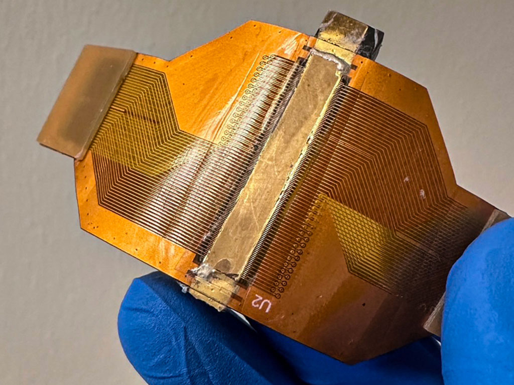 A blue-gloved hand flexes a small orange wearable sensor, with conductive traces on the circuit board.