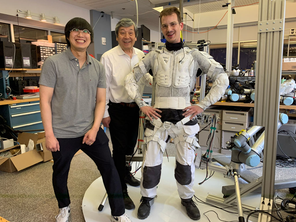 Two photos show Erik wearing the unique astronaut suit, from the side and from the back. The suit is like an open metal backpack full of wires and equipment and with legs.