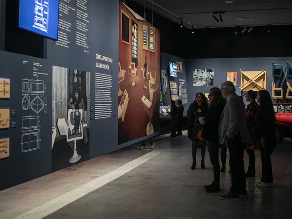 Several people in a dimly lit exhibit hall stop to read a panel at the exhibit's grand opening.